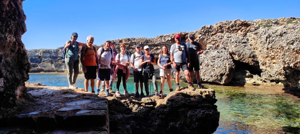 CAMÍ DE CAVALLS-Etapa10:Cap d'Artrutx-Cala Galdana . Caminando por Mallorca Grupo de ocho personas posando en una formación rocosa junto a aguas cristalinas, con un paisaje costero al fondo.