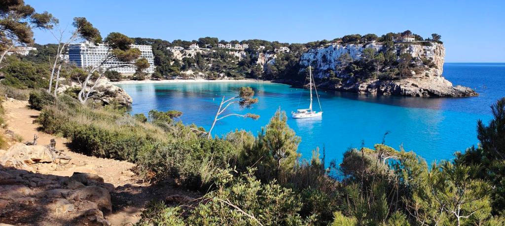 CAMÍ DE CAVALLS-Etapa10:Cap d'Artrutx-Cala Galdana . Caminando por Mallorca Vista panorámica de Cala Galdana con aguas turquesa, un barco a vela y acantilados rodeados de vegetación.