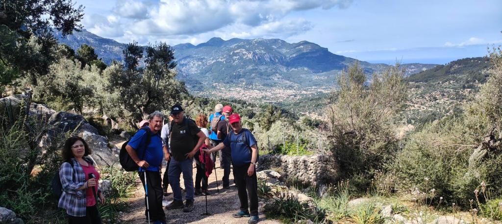 Grupo de excursionistas en un camino rodeado de naturaleza, con vistas a un valle y montañas en el fondo.