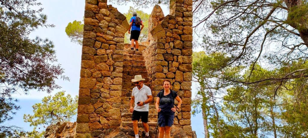 Grupo de personas subiendo una escalera en una torre de piedra rodeada de árboles en la ruta Miradores del Archiduque 2 en Mallorca.