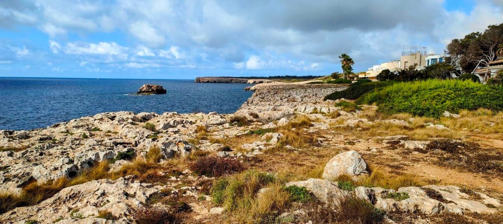 Vista de la costa virgen de Mallorca, con formaciones rocosas y el mar al fondo, bajo cielos nublados.