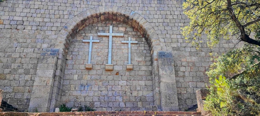 Conjunto monumental de Ses Tres Creus, con tres cruces de piedra en relieve en un arco de triunfo, en un entorno natural con vegetación.