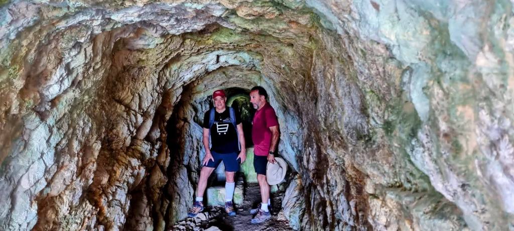 Dos personas dentro de una mina en un túnel excavado en roca, con paredes irregulares y iluminadas de manera natural.