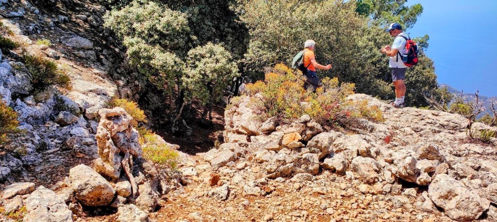 Dos senderistas en lo alto del Pas de sa Rata. un paisaje rocoso con vegetación, observando el entorno desde un punto elevado.