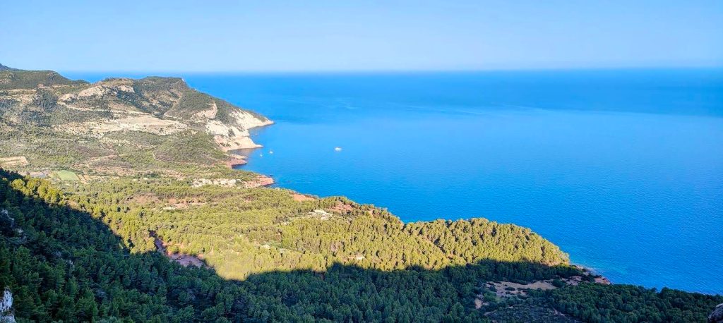 Vista panorámica de la costa de Mallorca, con formación montañosa y vegetación típica en primer plano y mar azul en el fondo.