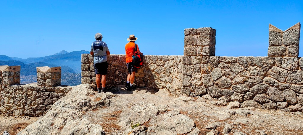 Dos personas observando el paisaje desde el Mirador de Ses Puntes, con un cielo despejado y montañas a lo lejos.