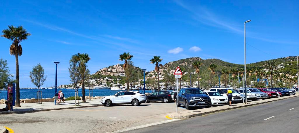 Vista del aparcamiento en el Puerto de Andratx, con coches estacionados y palmeras al fondo, frente al mar y montañas.