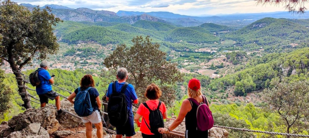 Grupo de personas disfrutando de la vista panorámica desde un mirador en la ruta 'Cor de Jesús-Ermita de Maristella' en la Sierra de la Tramontana, Mallorca, rodeados de vegetación y montañas.