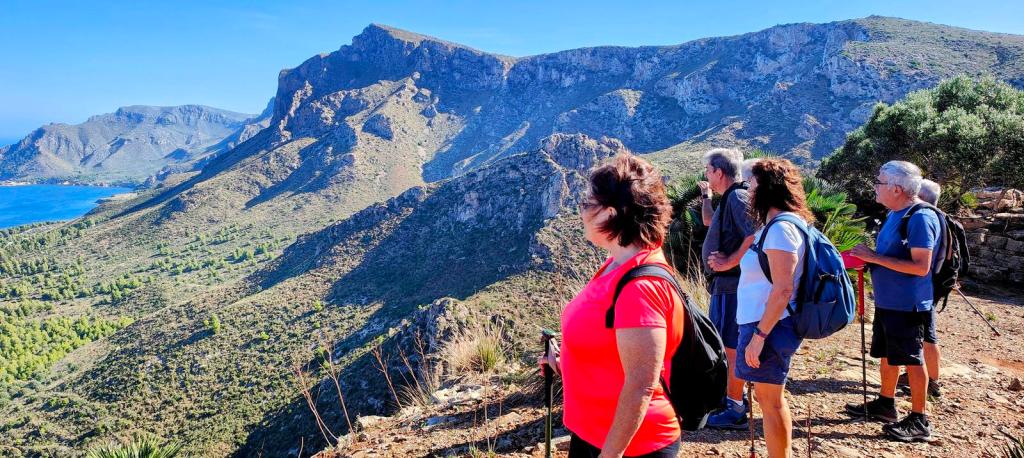 Grupo de personas en un sendero montañoso, observando el paisaje de la Serra de Llevant en Mallorca, con montañas y el mar visible en el fondo.