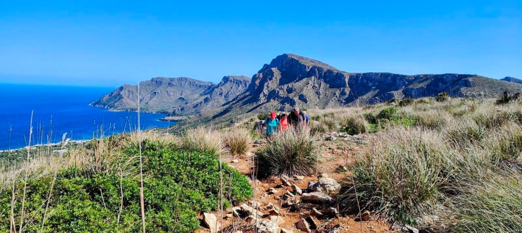 Grupo de senderistas caminando por un sendero montañoso con vistas al mar y a las montañas en la Serra de Llevant, Mallorca.