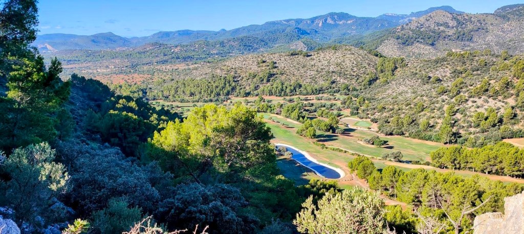 Vista panorámica del Campo de Golf de Son Termes, rodeado de colinas y vegetación, con montañas al fondo.