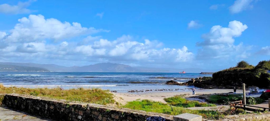 Vista panorámica del océano Atlántico con nubes dispersas y una playa de arena en primer plano, situada en la ruta "Cruceiro Marco de Couto-San Roque".