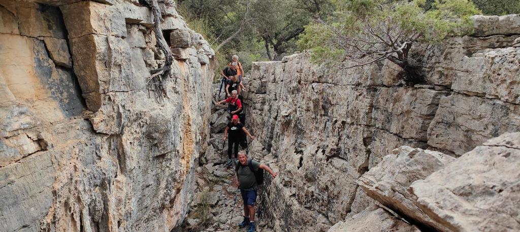 Fesa Costitxa-Font de la Coma desde Puigpunyent - Caminando por Mallorca Grupo de personas caminando a través de una grieta en una formación rocosa en la ruta 'Fesa Costitxa-Font de la Coma'.