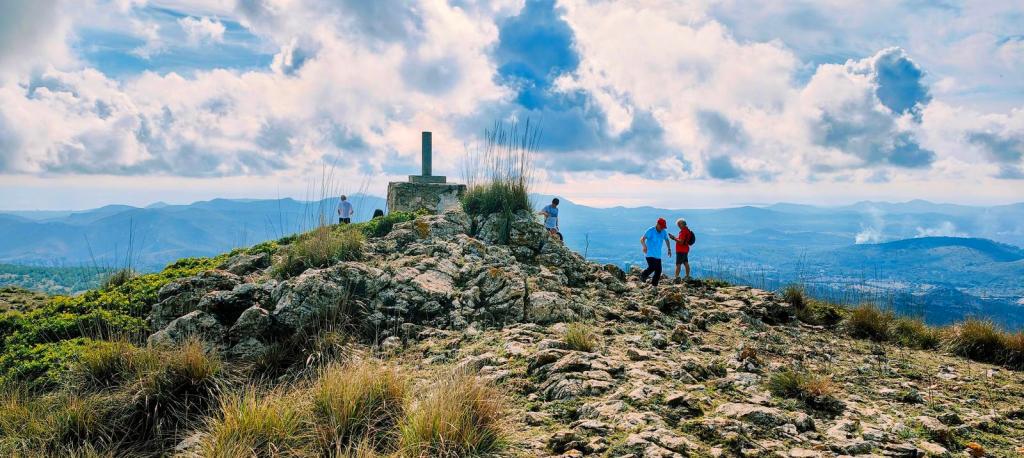 Grupo de personas en la cima de Sa Talaia Freda, con vistas panorámicas de montañas y nubes en el fondo.