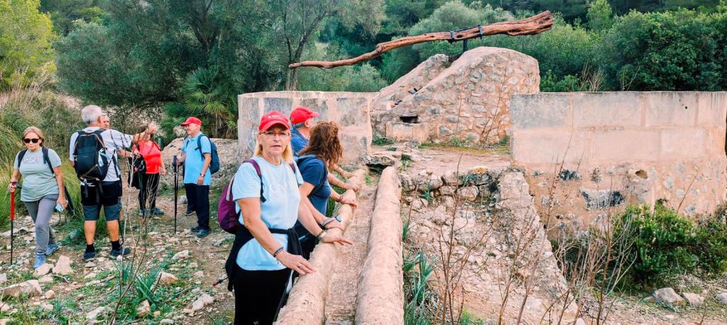 Grupo de senderistas en un camino junto a una antigua estructura de piedra, rodeados de vegetación, mientras exploran la Ruta 'Sa Talaia Freda' en Mallorca.