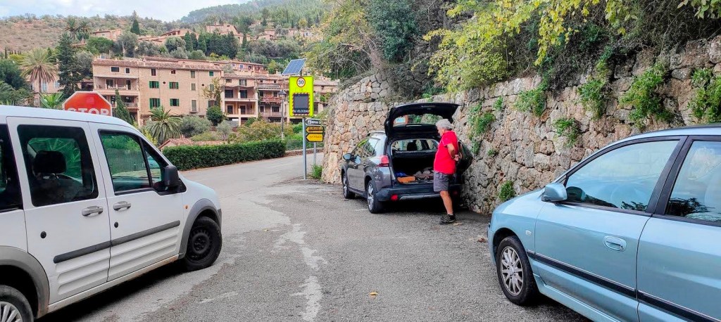 Puig de la Galera-Pas de Can Boqueta - Caminando por Mallorca Un hombre está organizando su coche en un pequeño aparcamiento cerca de un camino que conduce a Deià, con varias casas y vegetación al fondo.