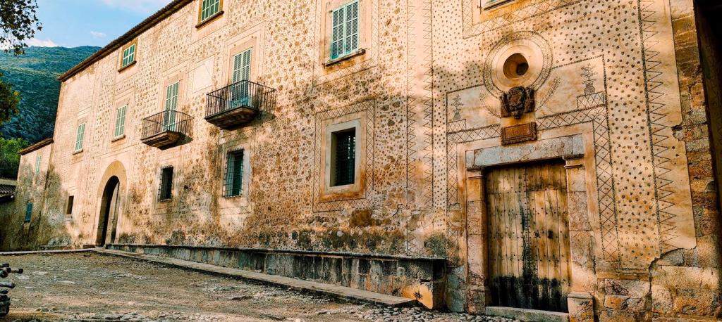 Fachada de un edificio histórico con decoraciones en piedra y ventanas verdes, ubicado en un entorno montañoso.