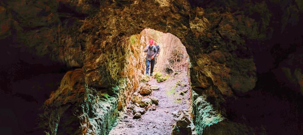 Vista de una persona caminando a través de una cueva con paredes rocosas y un camino de tierra en el interior.