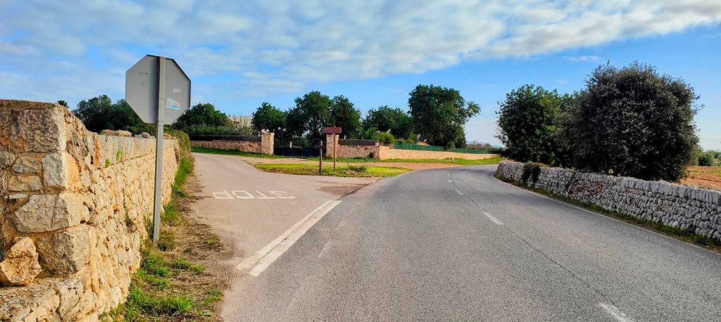 Vista de un cruce en la carretera, con señal de alto y un paisaje rural al fondo, rodeado de piedras y vegetación.