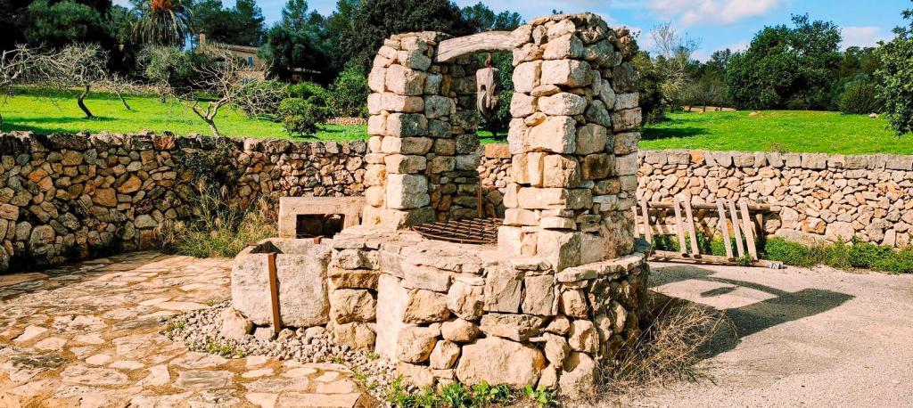 Un pozo de piedra rectangular cubierto con una rejilla metálica, rodeado de un área verde y muros de piedra, en un entorno rural.
