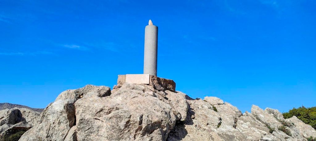 Puig del Tossals Verd desde Cúber - Caminando por Mallorca Monolito en la cima del Puig dels Tossals Verd, rodeado de rocas y un cielo azul claro.