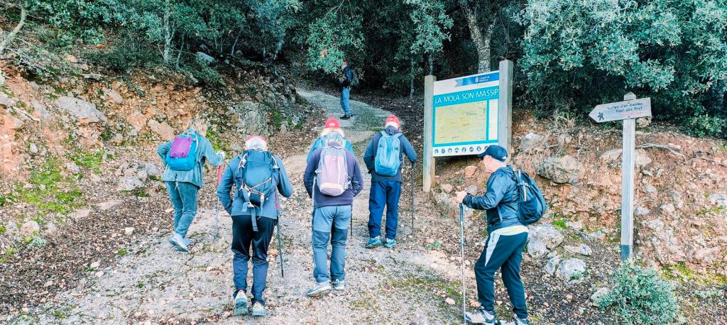 Grupo de excursionistas caminando por un sendero en la Serra de Tramuntana, con un panel informativo sobre la ruta 'Casa de Neu de Galileu desde Son Massip' al lado.