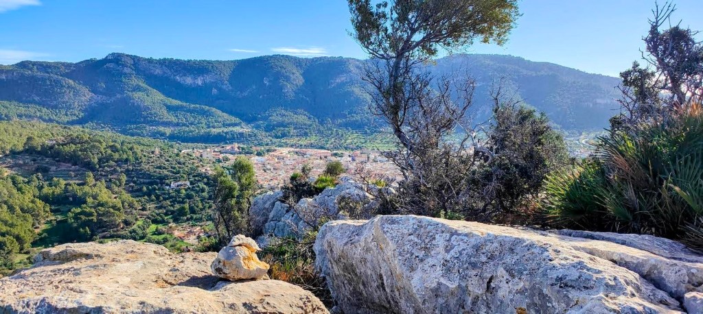 Vista panorámica desde una cima, mostrando montañas y un valle con vegetación típica, rodeado de rocas y arbustos.