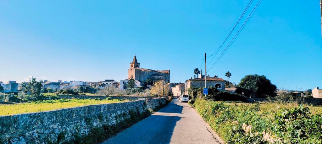 Ruta Hidráulica 3 de Porreres - Caminando por Mallorca Vista de un camino que lleva hacia el pueblo de Porreres, con una iglesia al fondo y edificios a los lados, bajo un cielo azul despejado.