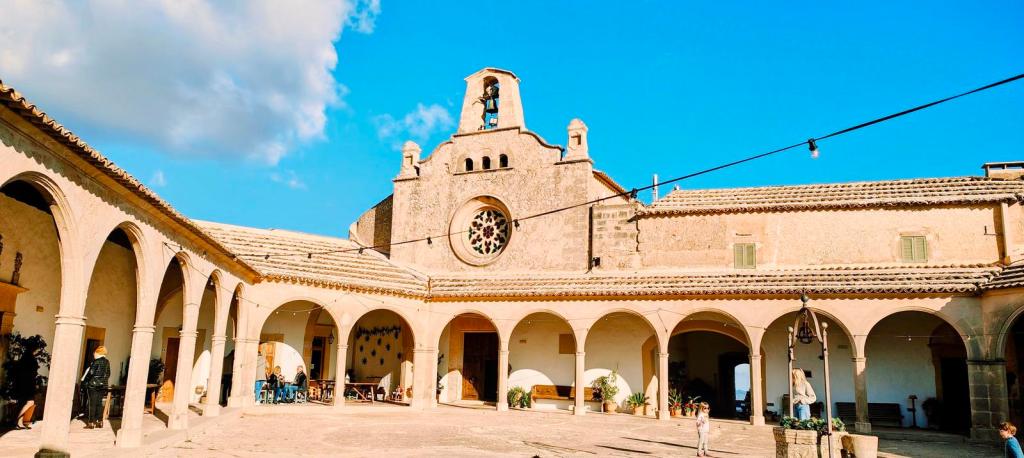 Vista del patio del Santuario de Monti-sion, con arcos y una torre campanario al fondo, bajo un cielo despejado.