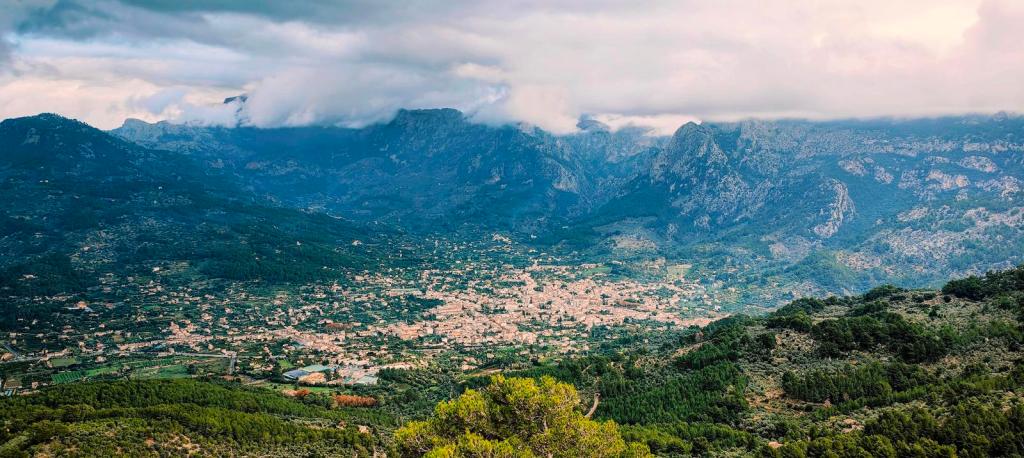 Vista panorámica del Valle de Sóller, rodeado de montañas y nubes bajas, con una mezcla de áreas urbanas y naturales.