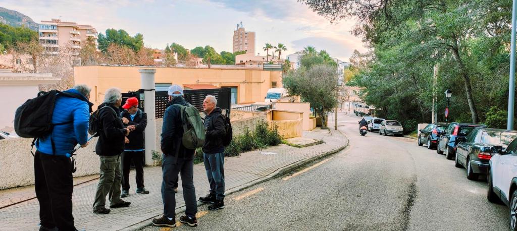 Grupo de personas preparándose para comenzar una ruta de senderismo en una calle de Peguera, con árboles y edificios de fondo.