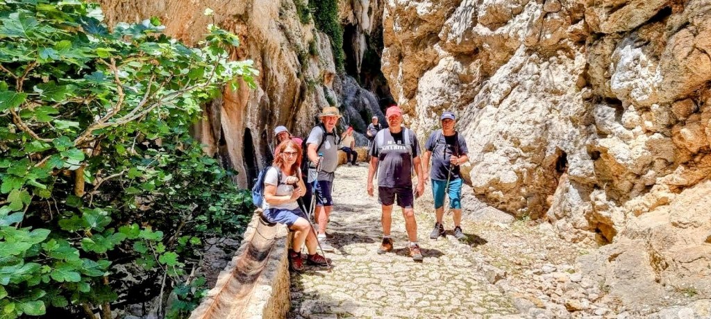 Font d’Es Verger desde Biniaraix - Caminando por Mallorca Grupo de excursionistas posando en un sendero estrecho rodeado de rocas y vegetación.