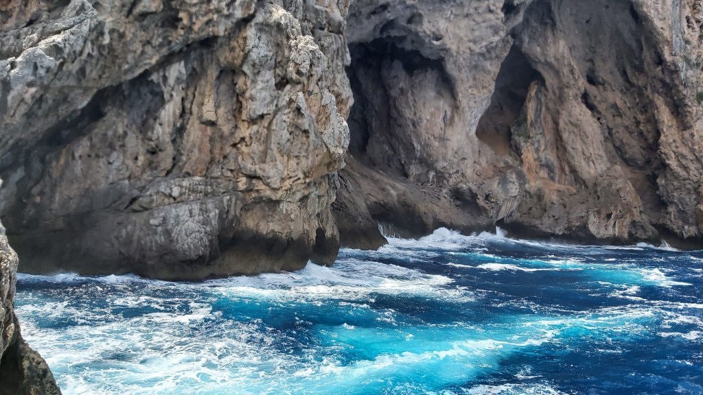 Vista de formaciones rocosas junto al mar, con olas rompiendo contra las rocas en un entorno natural.