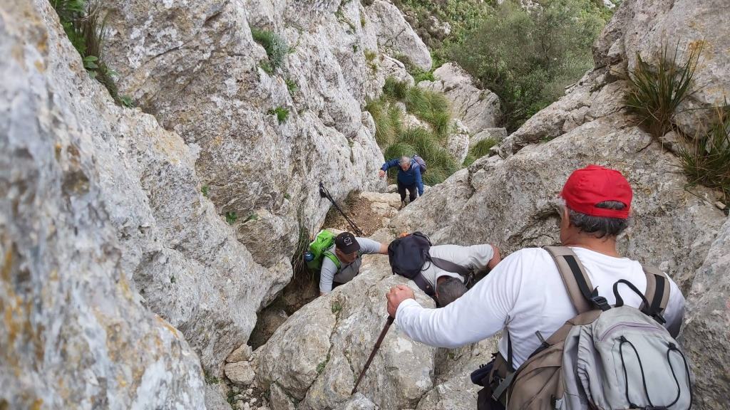 Grupo de senderistas descendiendo por el  Pas de l’All entre rocas durante la ruta Cuculla de Fartàritx.