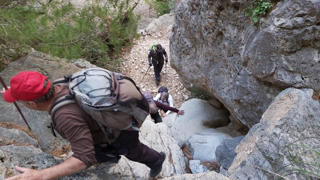 Senderistas ascendiendo por un tramo rocoso del Barranco de sa Gubia, rodeados de piedras y vegetación.