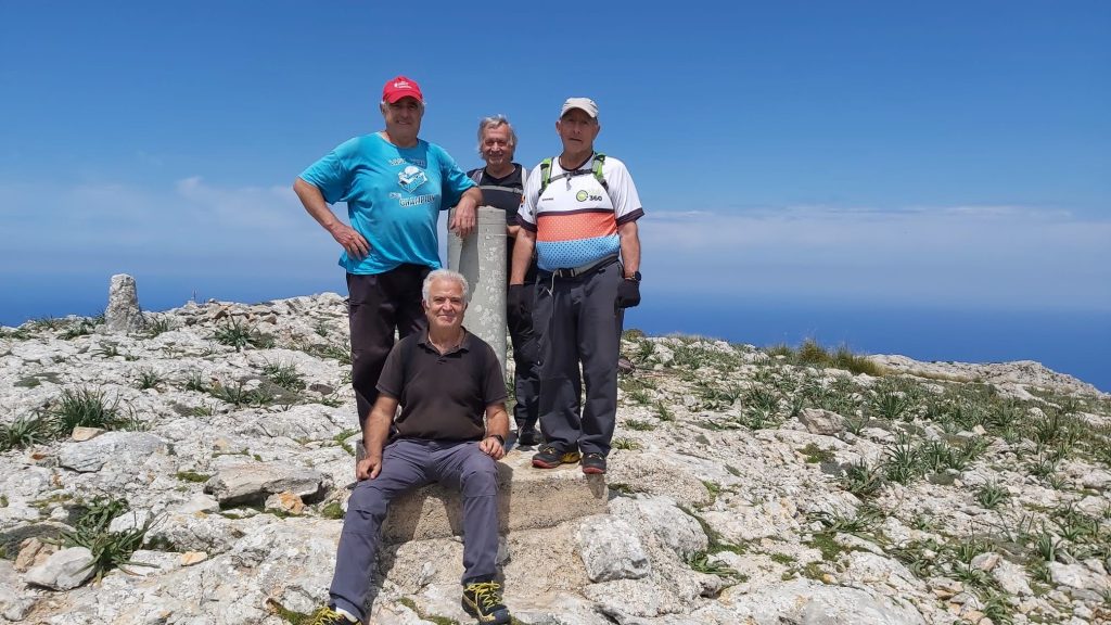 Grupo de personas en la cima de la Mola de s'Esclop, rodeados de un paisaje montañoso y con un vértice geodésico visible.