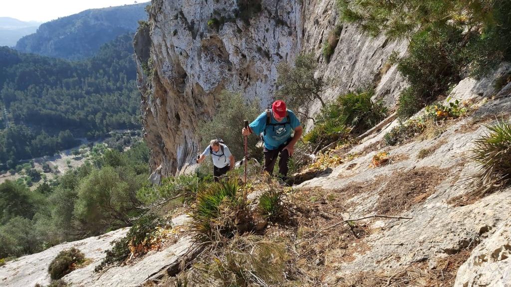 Dos senderistas ascendiendo por el Pas d'en Galeri, con un paisaje montañoso y vegetación de fondo.