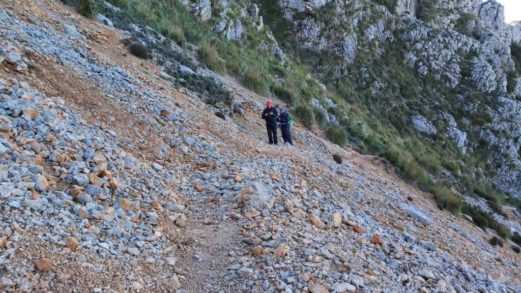 Grupo de excursionistas en una "Rossaguera" durante la ruta hacia el Puig Tomir, con vegetación y pared montañosa al fondo.
