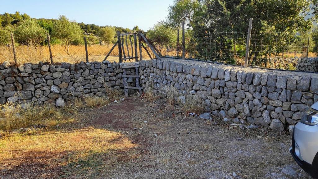 Botador de madera situado sobre un muro de piedra, con un área de tierra y vegetación alrededor, en un paisaje rural de Mallorca.