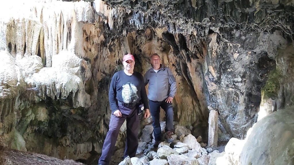 Dos hombres de pie dentro de la Cova de s' Alfàbia con formaciones rocosas minerales en las paredes.