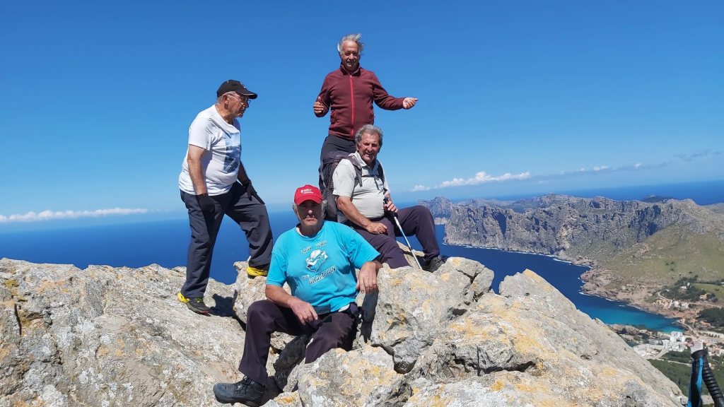 Grupo de cuatro personas en la cima del Puig de Cornavaques, disfrutando de vistas panorámicas al mar y la costa de Mallorca.