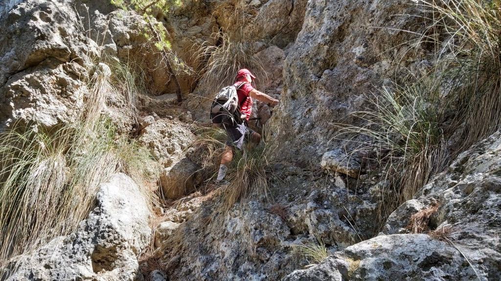 Un excursionista subiendo por Pas des Moros, 
una empinada canal de rocas cubiertas de hierba, en un entorno natural montañoso.