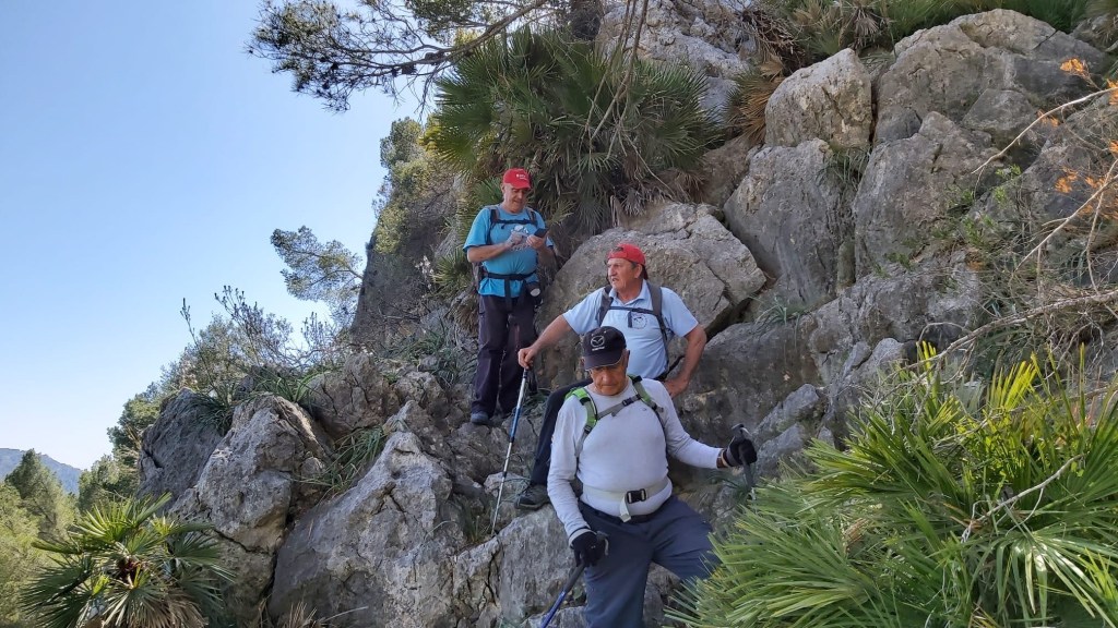 Tres senderistas descendiendo por el Pas de s’ Arna en la ruta Puig de Son Monjo, rodeados de vegetación.