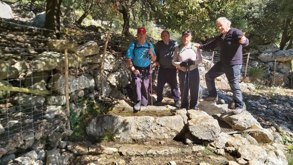 Cuatro excursionistas descansan sobre una roca en un sendero montañoso, rodeados de árboles y naturaleza durante su ruta en la zona de Orient.