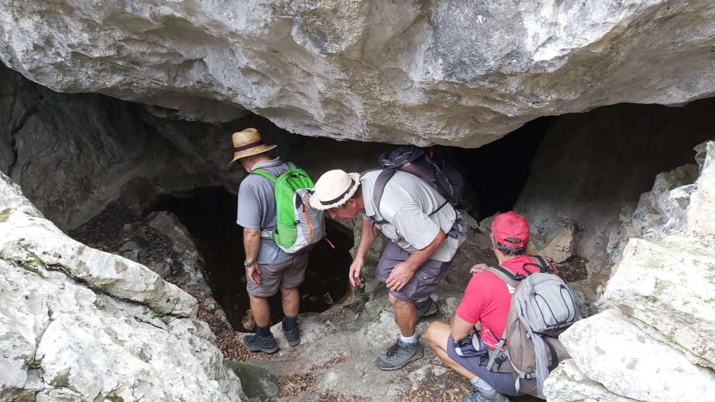 Grupo de excursionistas explorando la entrada de la Cova dels Ermassets rodeados de rocas y vegetación.