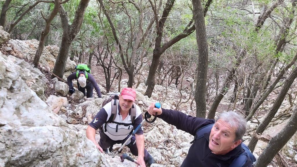 Grupo de senderistas ascendiendo por el Passet de la Cova Morella, rodeados de árboles y matorrales.