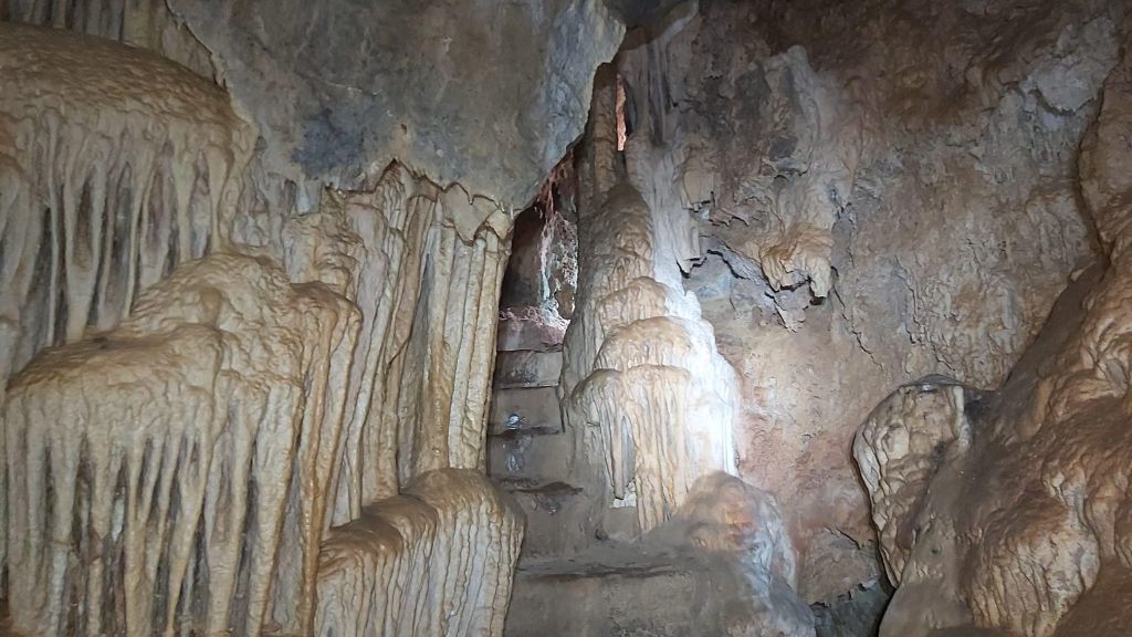 Cova Tancada-Playa del Coll Baix-Caminando por Mallorca Interior de la Cova Tancada, mostrando formaciones kársticas como estalagmitas y estalactitas en un entorno rocoso y húmedo.