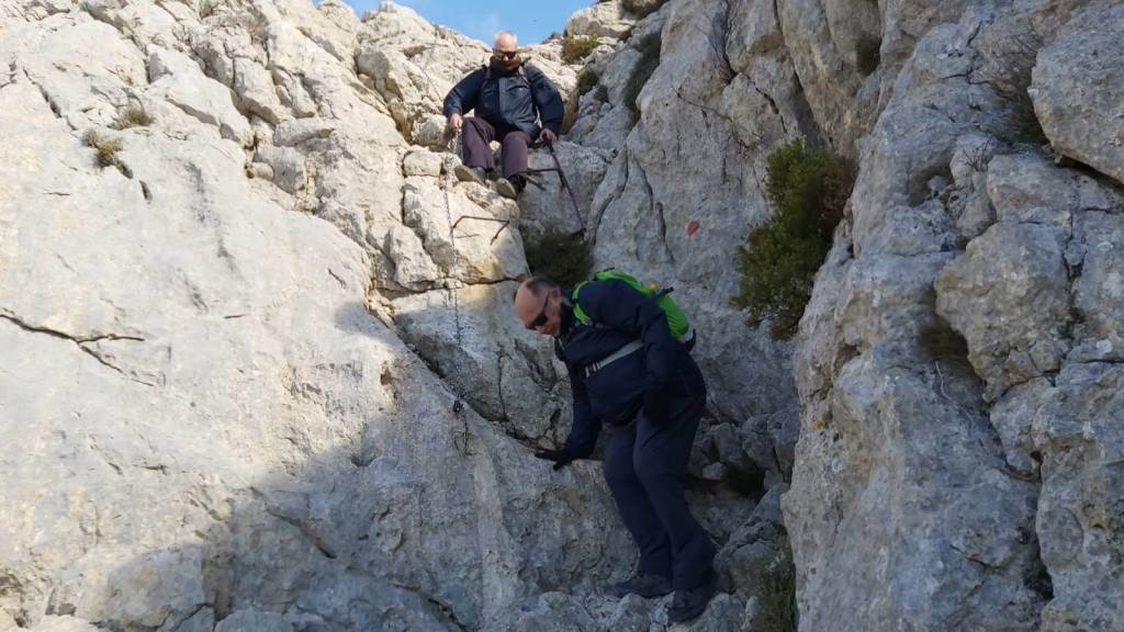 Hombres descendiendo por el Pas des Pedregaretdurante la ruta de senderismo hacia el Puig Tomir, con un paisaje de rocas y vegetación alrededor.