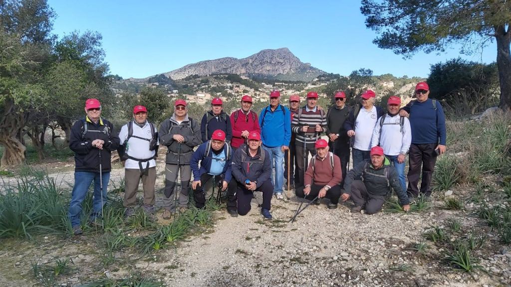 Grupo de senderistas posando en un sendero con montañas al fondo, todos llevan gorras rojas.