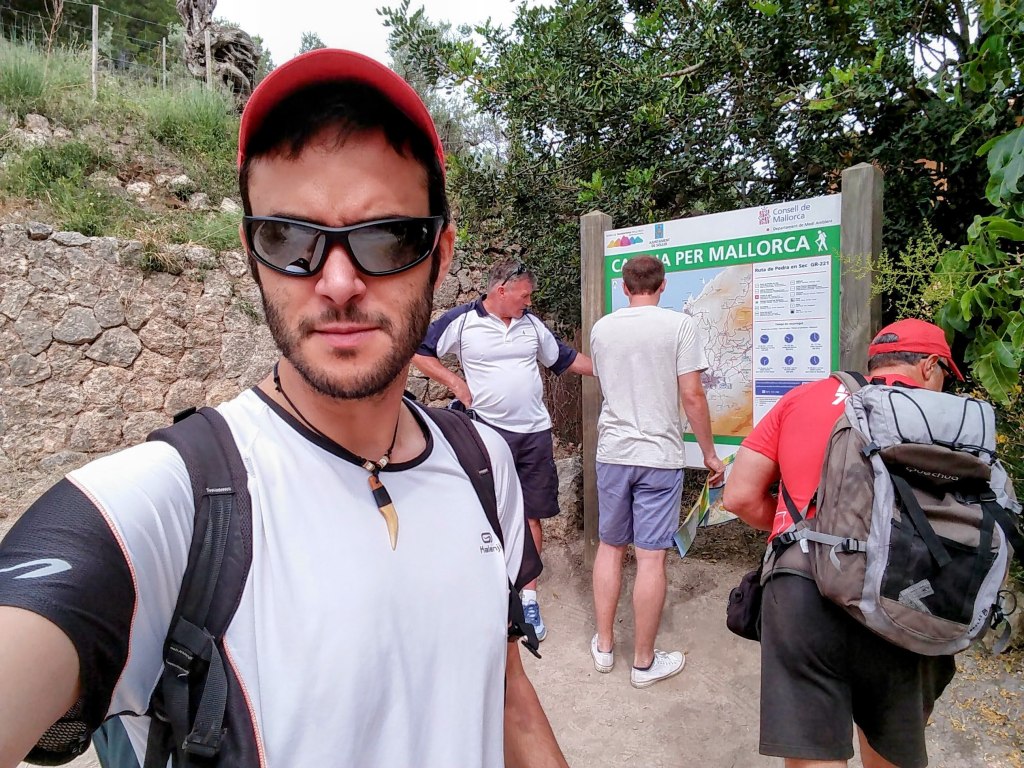 Grupo de excursionistas revisando un mapa en el inicio de la ruta 'Puig des Moro por el Pas d’en Jeroni Gros', rodeados de vegetación.